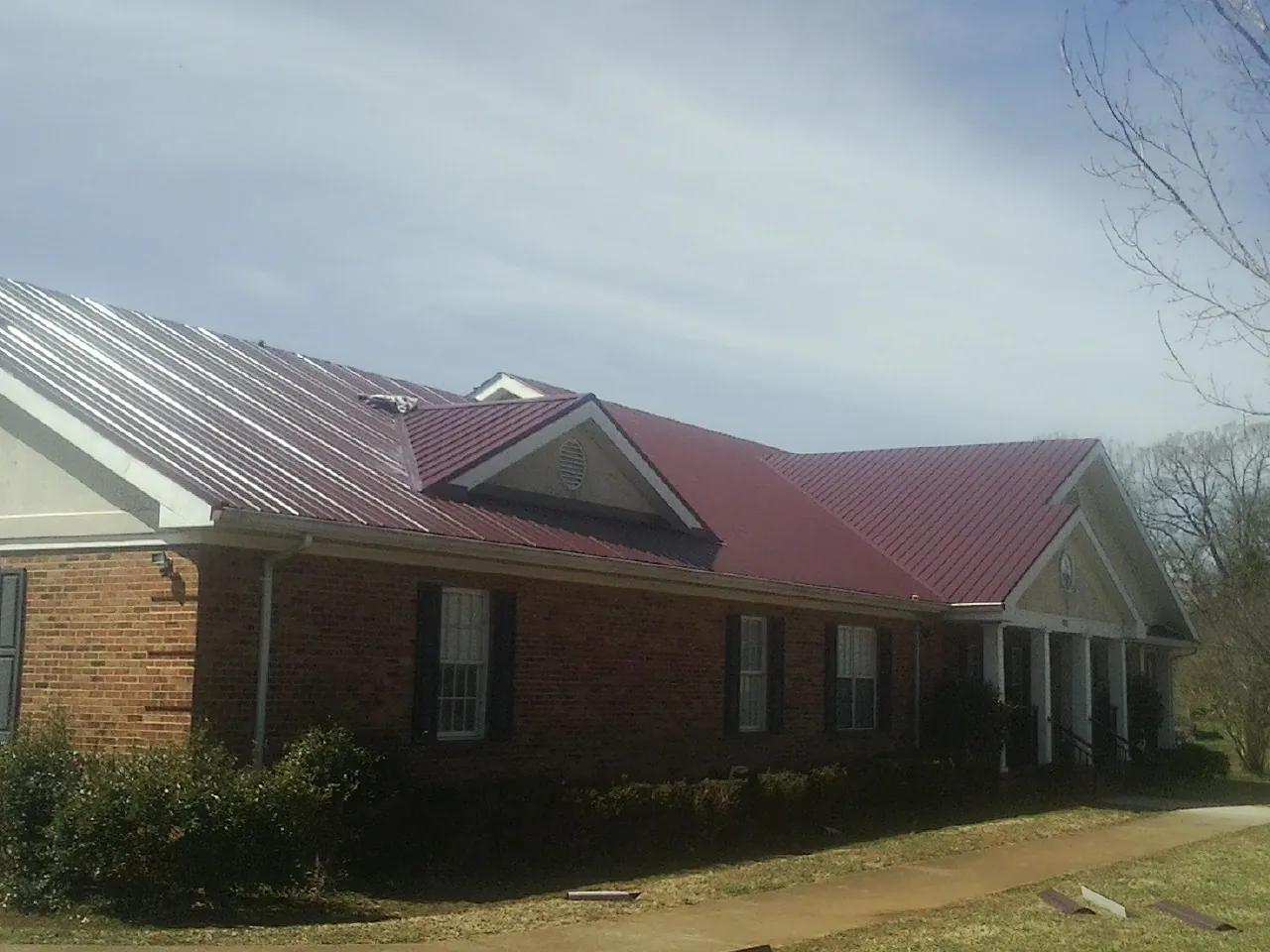 Red metal roof with gabled entries on a long brick building, from a Hail Damage Roof Repair job in Boiling Springs